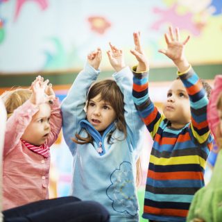 Cute children playing in the playroom with their arms raised.