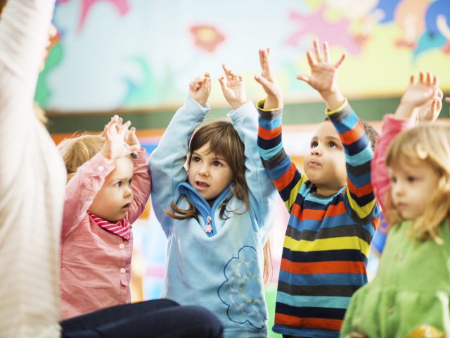 Cute children playing in the playroom with their arms raised.